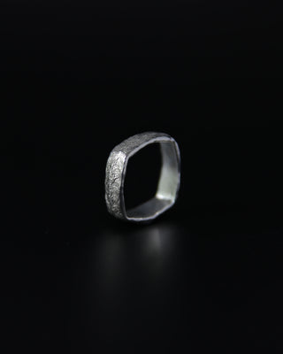 Silver ring with textured design on a black background