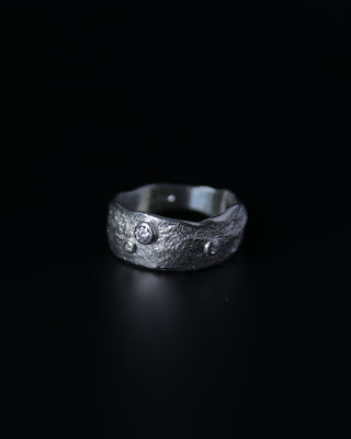 Silver ring with textured band and embedded moissanite stones on a black background