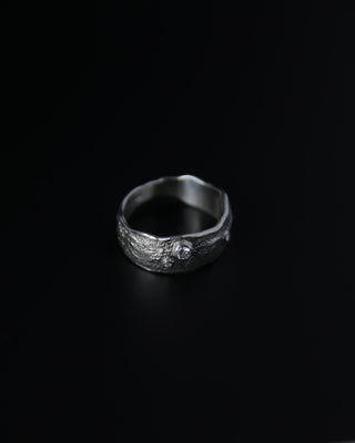 Silver ring with a textured band and central gemstone on a black background