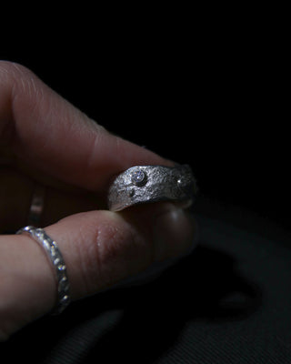 Hand holding a moissanite and sterling silver ring with a dark background