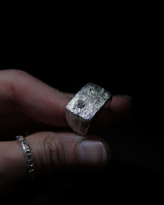 Hand holding a sterling silver moissanite signet ring against a dark background
