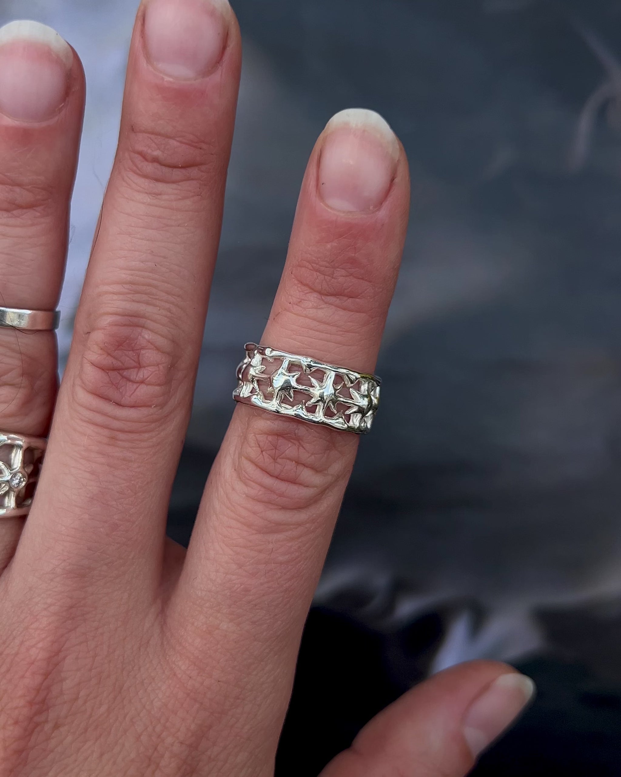 Showcase of a sterling silver ring with intricate star details on a hand with roman sculpture as a background